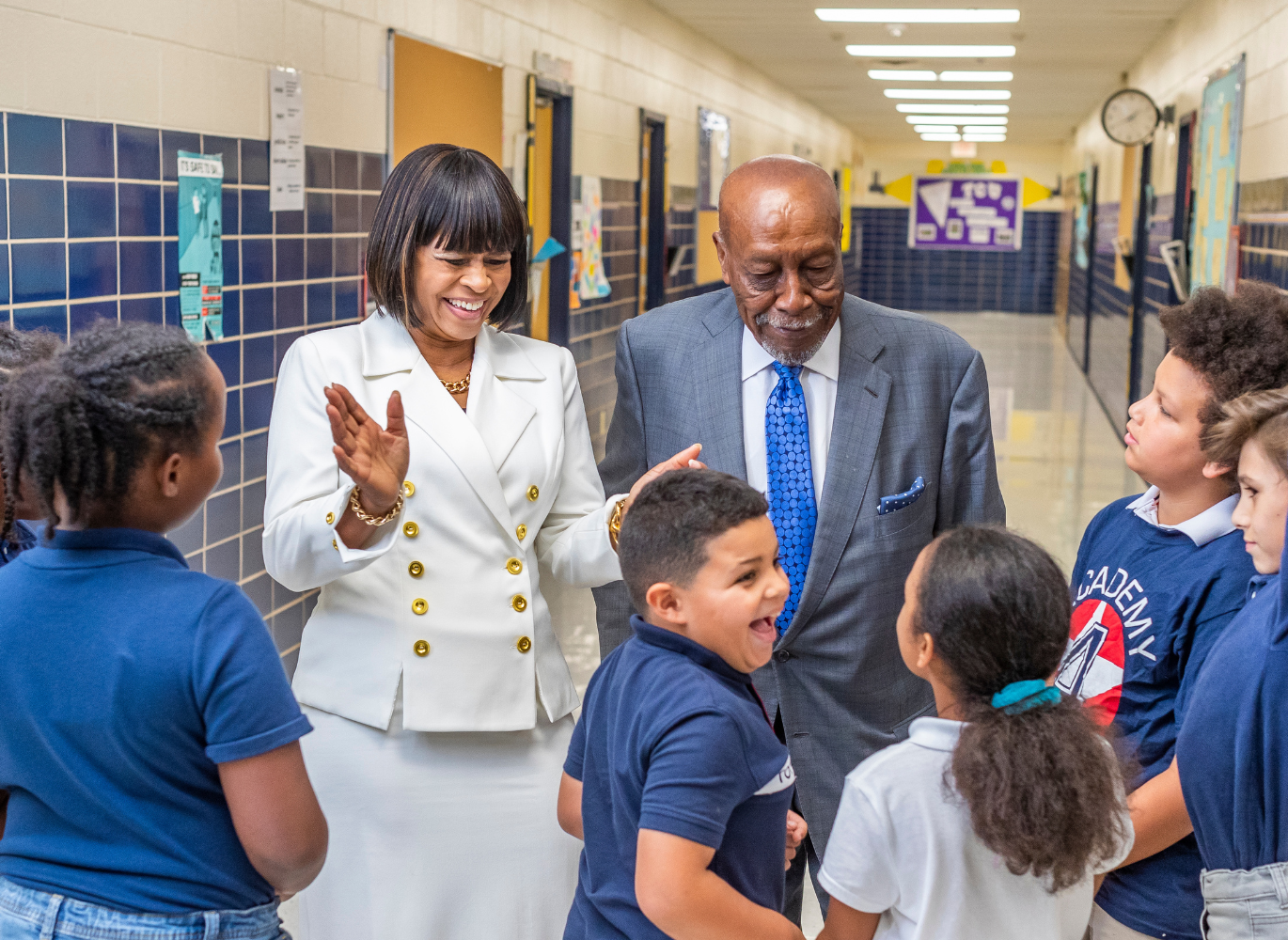 Photo of a man and woman visiting a school talking to a group of students